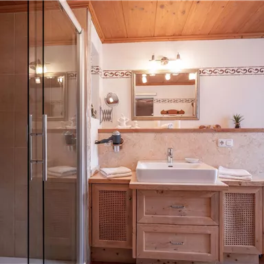 Ein modernes Badezimmer mit Holzdecke, einer Dusche und einem eleganten Waschbecken. Die Einrichtung ist schlicht und stilvoll, mit dekorativen Elementen.