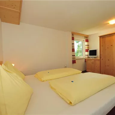 Ein gemütliches Schlafzimmer mit zwei Betten und gelben Kissen. Der Raum hat Holzdetails und einen Fernseher auf einem Schreibtisch.