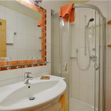 A modern bathroom with a shower and a sink. A decorative mirror hangs on the wall and there are wooden shelves.