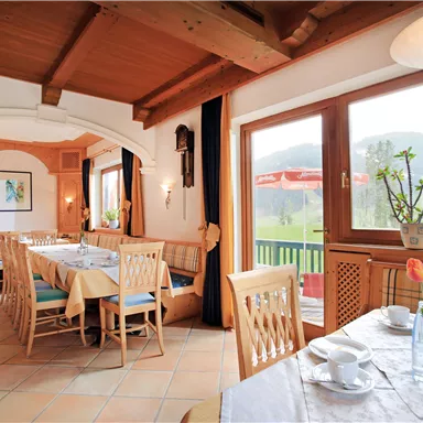 A cozy restaurant with a wooden ceiling and large windows. Tables are set and offer a view of the green landscape outside.