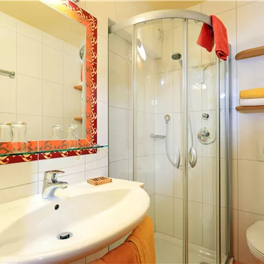 A modern bathroom with a shower and a sink. The walls are brightly tiled and there are orange towels.