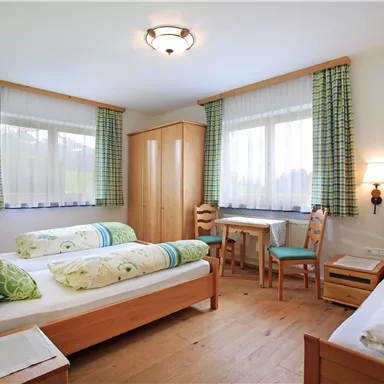 A bright room with two single beds and a desk. The large windows provide plenty of daylight and a view of the surroundings.