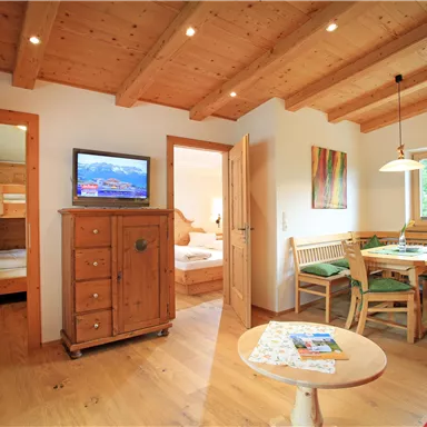 A cozy living space with wooden ceilings and modern furniture. There is a table, chairs, and a television in the center of the room.