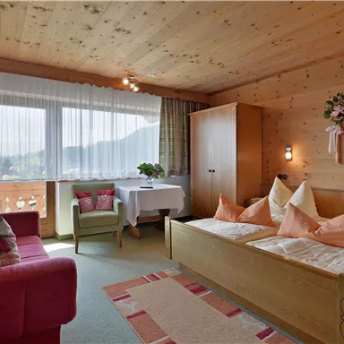Ein gemütliches Zimmer mit Holzwänden, einem Doppelbett und einem roten Sofa. Große Fenster bieten einen Ausblick auf die Landschaft.
