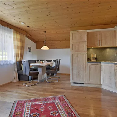 Eine helle Wohnung mit Holzbalkendecke und modernem Mobiliar. Der Raum beinhaltet eine Küche, einen Essbereich und ein gemütliches Ambiente.