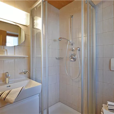 Ein modernes Badezimmer mit Dusche, Waschbecken und Spiegel. Die Wände sind hell gefliest, und frische Handtücher liegen bereit.