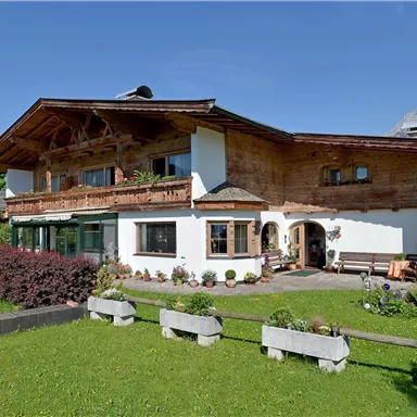 Ein traditionelles alpenländisches Haus mit Holzverkleidung und einem schönen Garten. Im Hintergrund sind die Berge sichtbar.