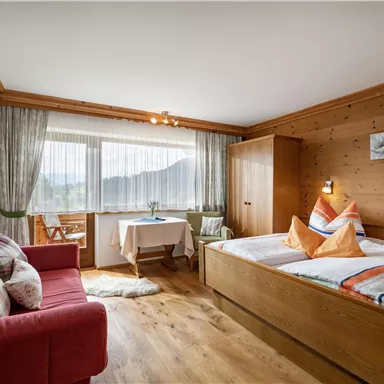 Ein gemütliches Schlafzimmer mit Holzverkleidung und großen Fenstern. Es gibt ein Doppelbett, eine gemütliche Sitzecke und einen Tisch mit Blick auf die Berge.