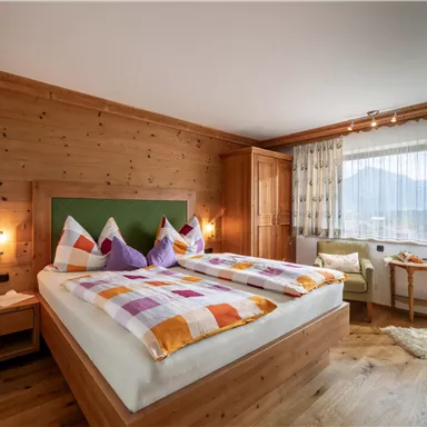 Ein gemütliches Schlafzimmer mit einem großen Doppelbett und bunten Kissen. Die Wände sind aus Holz, und es gibt ein Fenster mit Blick auf die Berge.