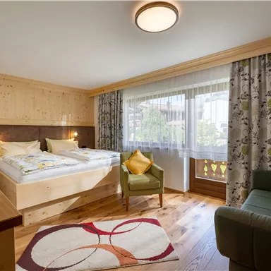 Ein gemütliches Zimmer mit zwei Betten und einem kleinen Sitzbereich. Große Fenster lassen viel Licht herein und die Dekoration ist modern und einladend.