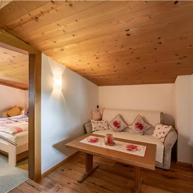 Eine gemütliche Sitzecke mit einem Tisch und einer Couch in einem Holzdekor-Raum. Im Hintergrund ist ein Schlafzimmer sichtbar.
