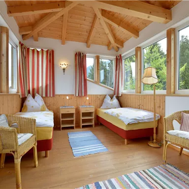 Ein gemütliches Zimmer mit zwei Betten und einem natürlichen Holzdach. Große Fenster bieten einen Blick ins Grüne und lassen viel Licht herein.