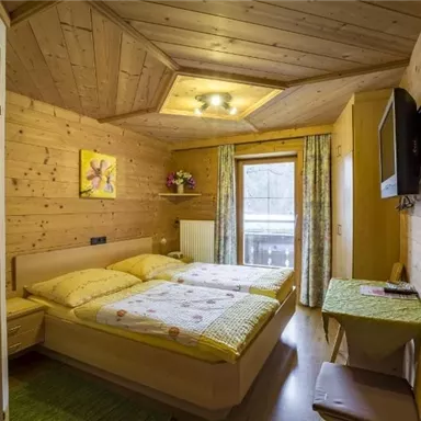 Ein gemütliches Zimmer mit Holzdekor und zwei Einzelbetten. Es gibt ein Fenster mit Zugang zu einem Balkon und einen Fernseher an der Wand.