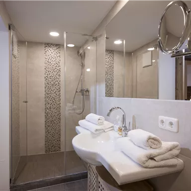 Ein modernes Badezimmer mit einer Glasdusche und eleganten Fliesen. Auf dem Waschbecken liegen frische Handtücher.