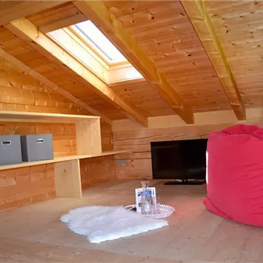 A cozy attic with wooden paneling and a large window area. A red seat cushion and a TV create an inviting atmosphere.