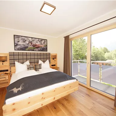 A cozy bedroom with a large bed and wooden furniture. The windows offer a view of the greenery.
