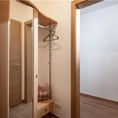 Ein heller Flur mit einem Spiegel und einem Kleiderständer. Die Wände sind neutral und der Boden ist aus Holz.