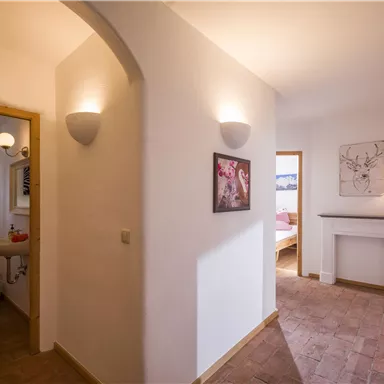 Ein heller Flur mit weißen Wänden und warmem Licht. Man sieht einen Zugang zu einem Badezimmer und einen Blick auf einen gemütlichen Wohnraum.
