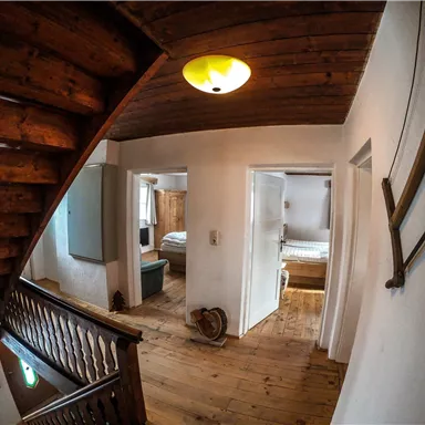 Ein heller Flur mit Holztreppe und rustikalem Ambiente. Die Wände sind weiß gestrichen und es gibt mehrere Türen zu angrenzenden Räumen.