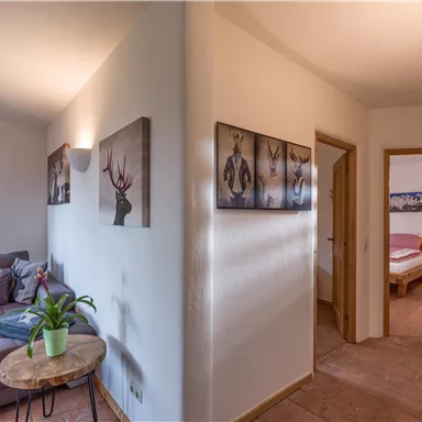 Ein heller Flur mit einer gemütlichen Sitzecke und Bildern an den Wänden. Durch eine Tür ist ein Schlafzimmer zu sehen.
