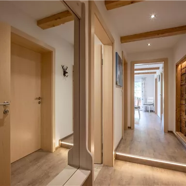 A bright hallway with wooden details and modern doors. Plenty of daylight is visible through the windows.