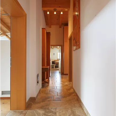 A bright hallway with modern tiles and wooden details. On the right side, there are doors leading to other rooms.