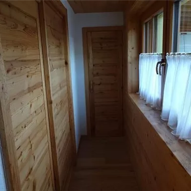 A bright hallway with wooden walls and a windowsill. Curtains and doors made of wood create a cozy atmosphere.