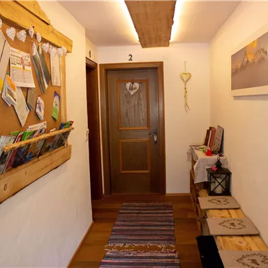 An inviting hallway with wooden elements and a bulletin board full of information. On the right, there is a table with decorations and some seating options.