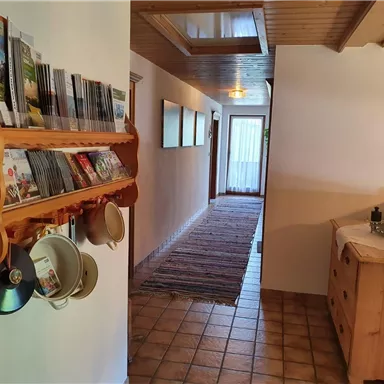 Ein geräumiger Flur mit Holzregalen für Broschüren und einer Kommode. Der Boden ist gefliest und ein Teppich verläuft den Gang entlang.