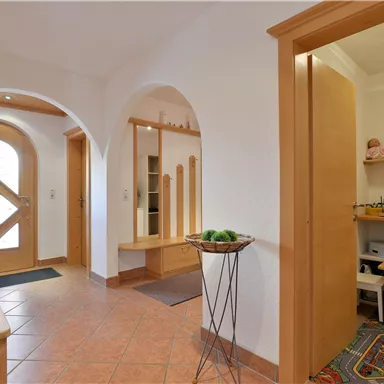 A bright hallway with wooden and tiled flooring. On the right side, there is a small room with toys and a table for children.