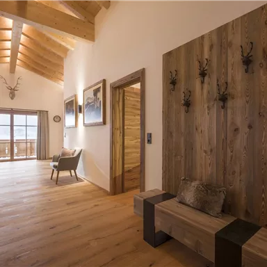 Ein freundlicher Eingangsbereich mit Holzverkleidung und großen Fenstern. Der Raum hat einen modernen, rustikalen Stil mit Holzfußboden und gemütlichen Möbeln.