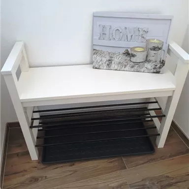 A white bench with storage compartments and a decorative sign "HOME" stands against the wall. Below it lies a black mat.