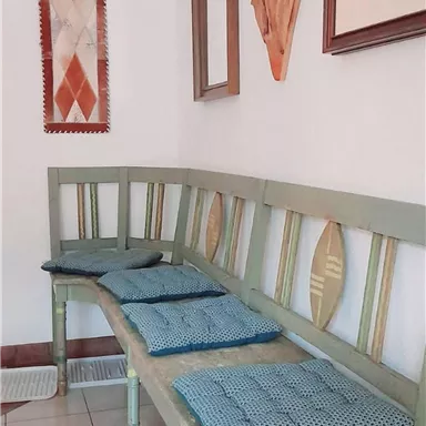 Eine gemütliche Bank mit blauen Kissen steht an der Wand. An der Wand sind dekorative Kunstwerke und ein Spiegel angebracht.