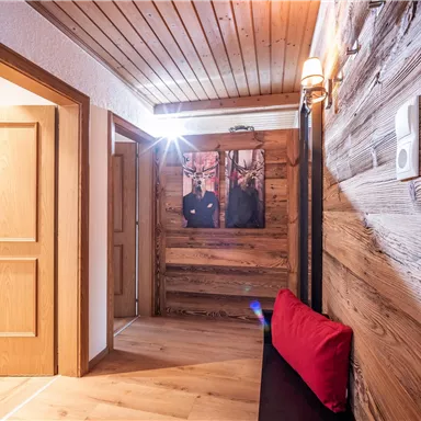 A cozy hallway with wooden paneling and a red cushion on a bench. A picture of two people hangs on the wall.