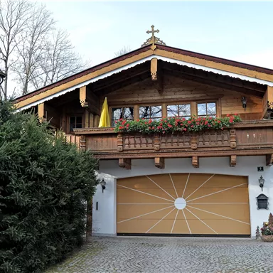 Ein traditionelles Chalet mit Balkon und Blumenkästen. Die Garage hat ein auffälliges, rundes Design.