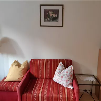 Ein gemütlicher Wohnbereich mit einem rot gestreiften Sofa und zwei Kissen. Neben dem Sofa steht eine Lampe und ein kleiner Tisch mit einer Kaffeekanne.