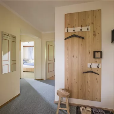 Ein heller Flur mit einem Holzpaneel und Kleiderhaken. Zu sehen sind ein Hocker und ein Spiegel.