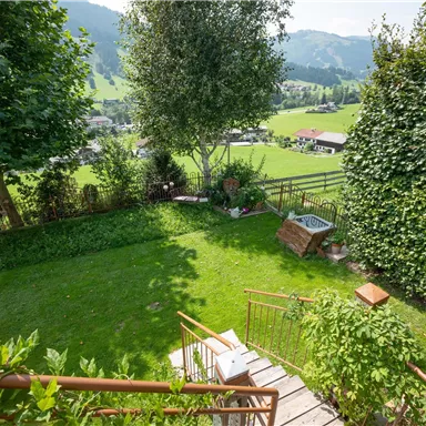 Eine sanfte Landschaft mit saftigem Grün und Bäumen. Im Hintergrund sind Berge und ein weitläufiges Feld zu sehen.