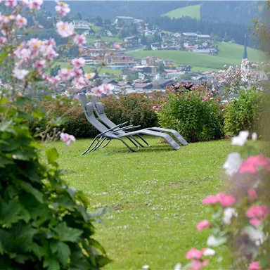 A beautiful garden with colorful flowers and a view of the city in the distance. In the foreground, there are two loungers on the lawn.