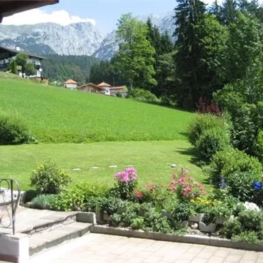 A green meadow with colorful flowers and mountains in the background. A peaceful and idyllic garden area.
