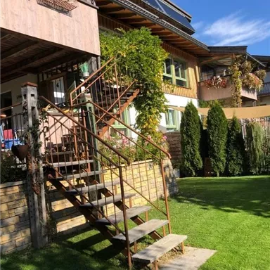 Ein gemütliches Haus mit einer rustikalen Treppe und gepflegtem Garten. Grünpflanzen und Blumen verleihen dem Außenbereich Farbe.