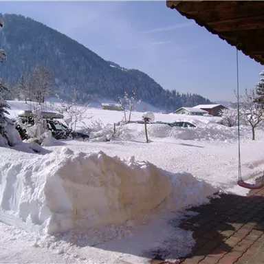 A snowy landscape with a mountain in the background. The sun is shining on the snow and there are tire tracks in the background.