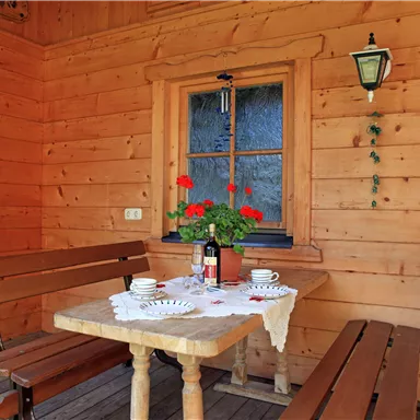 Ein gemütlicher Holzveranda mit einem Tisch und Bänken. Auf dem Tisch steht eine Blumenvase und Geschirr, umgeben von einer warmen, rustikalen Atmosphäre.