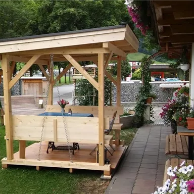 A cozy wooden gazebo in the garden with a table and chairs. Flowers and plants adorn the area around the gazebo.