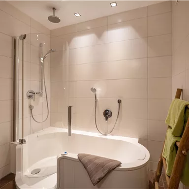 A modern bathroom with a comfortable bathtub and a separate shower. The walls are tiled in light colors, and there are some towels on a wooden shelf.