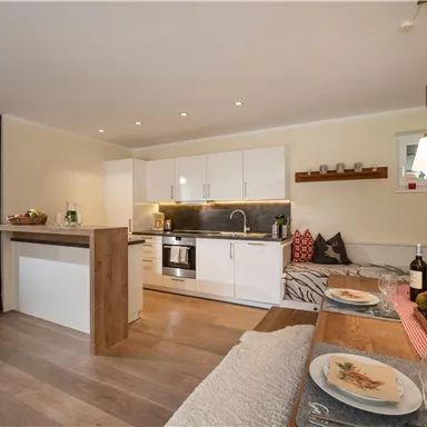 A modern and bright kitchen with white furniture and wooden details. Cozy seating area with table and decorative elements.