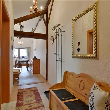 An inviting hallway with wooden beams and a cozy seating area. At the end of the hallway, a dining area is visible.
