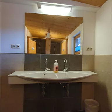 A modern bathroom with a large sink and a mirror. The walls are elegantly designed in neutral tones, and there are wooden ceiling elements.