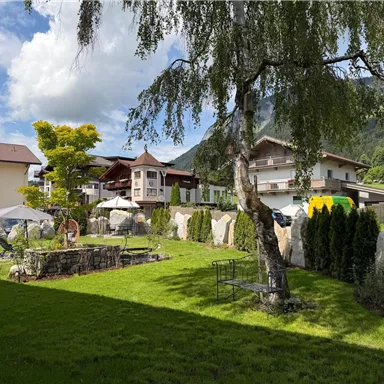 An idyllic landscape with a well-kept garden and a tranquil atmosphere. In the background, traditional houses and gentle hills can be seen.