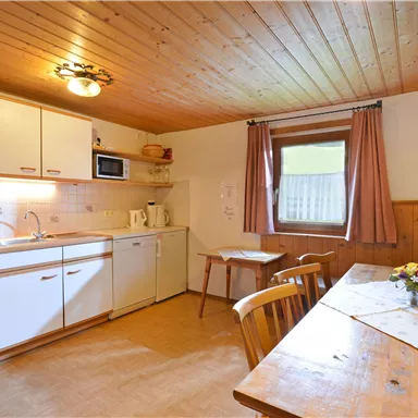 Eine helle Küche mit modernen Geräten und Holzverkleidung. Ein Tisch mit Blumenarrangement lädt zum Essen ein.